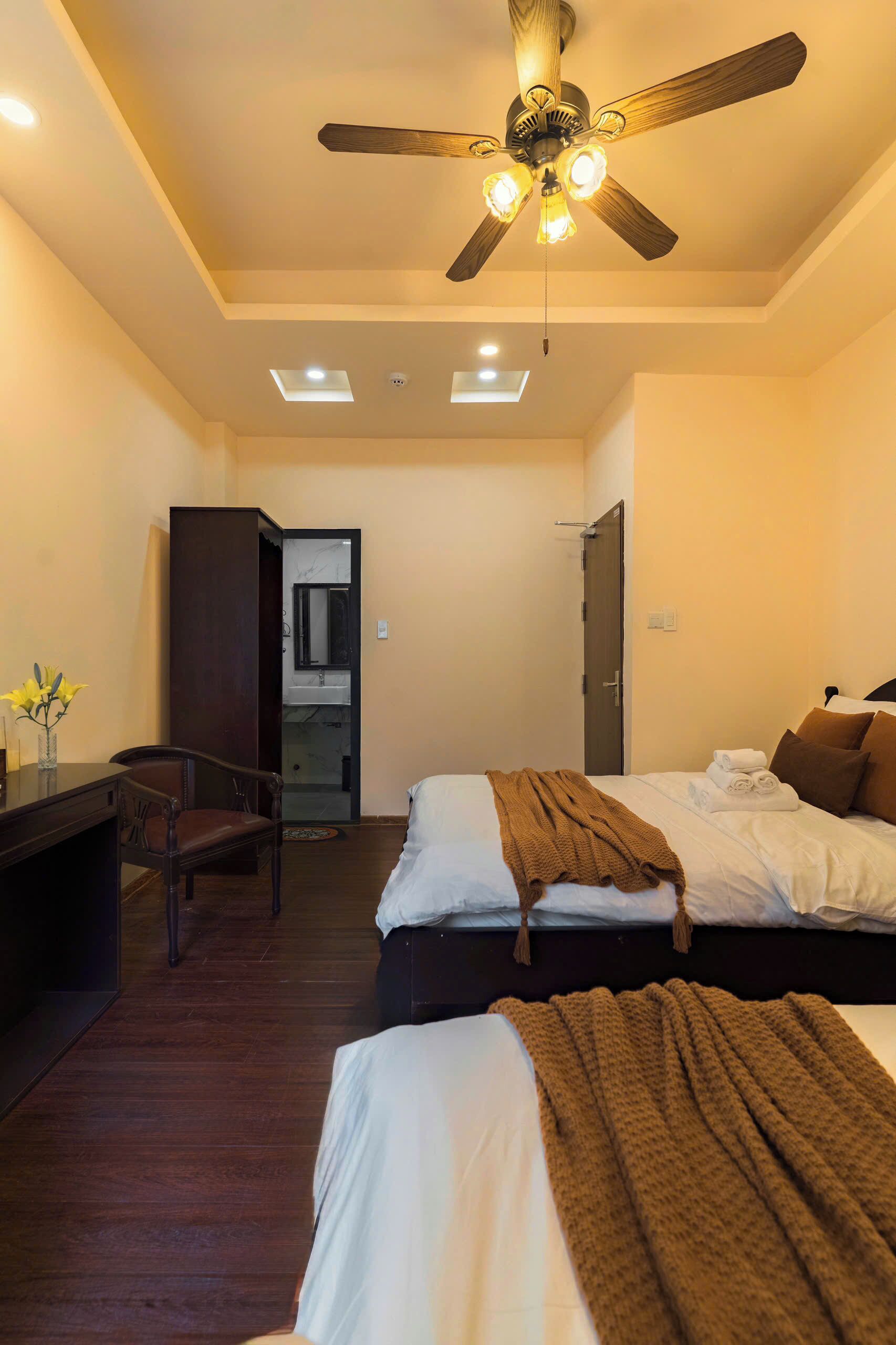 A hotel room with a ceiling fan, two beds, a desk, and a bathroom visible through an open door.