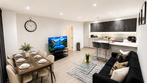 A modern living room with a dining area, a kitchen, and a TV displaying a scenic landscape.