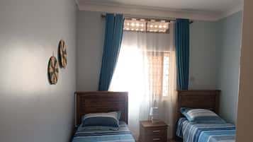Une chambre avec deux lits simples, une table de chevet, une fenêtre avec des rideaux et un plancher en bois.