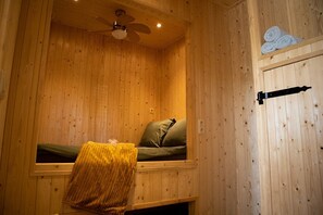 Ein Zimmer aus Holz mit einem Bett, einem Deckenventilator und einem Handtuchhalter.