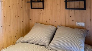 Una habitación con paneles de madera, una cama, dos estantes en la pared y una lámpara en el techo.