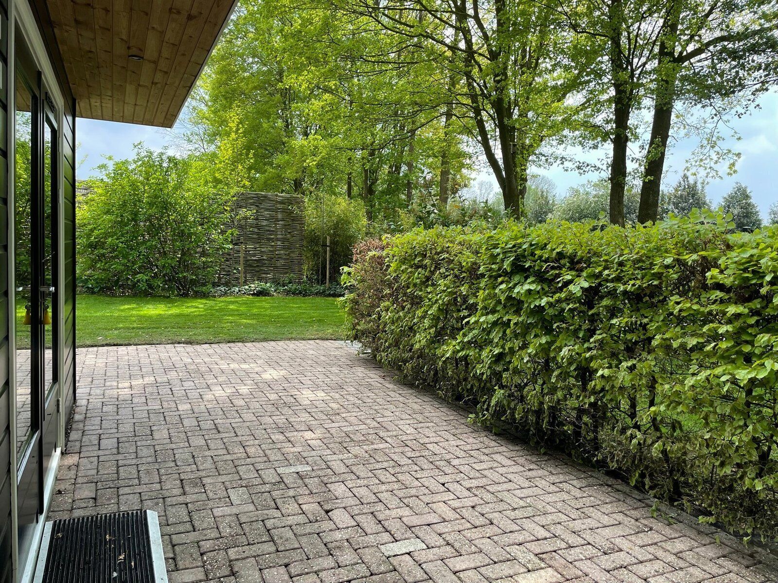 A paved pathway leading to a building with a wooden roof, surrounded by lush greenery and trees.