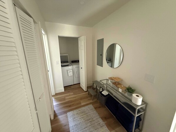 A hallway with a laundry area, a mirror, and a small table with a plant and a roll of toilet paper. - Cozy 3BR Ranch Near Blacklick Woods, Columbus (Reynoldsburg)
