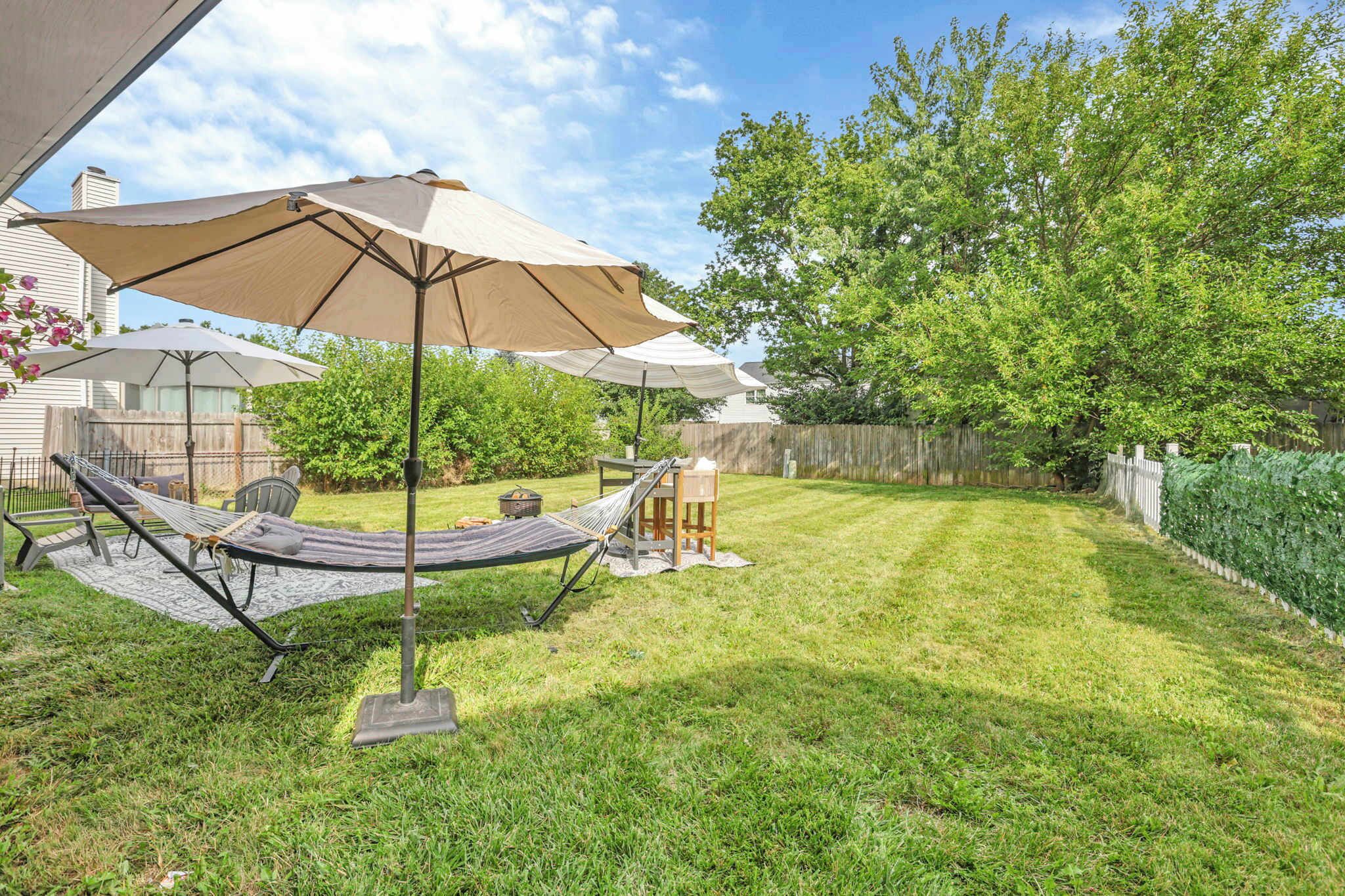 A backyard with a hammock, a table, and a chair under a large umbrella.