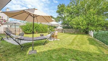 A backyard with a hammock, a table, and a chair under a large umbrella.