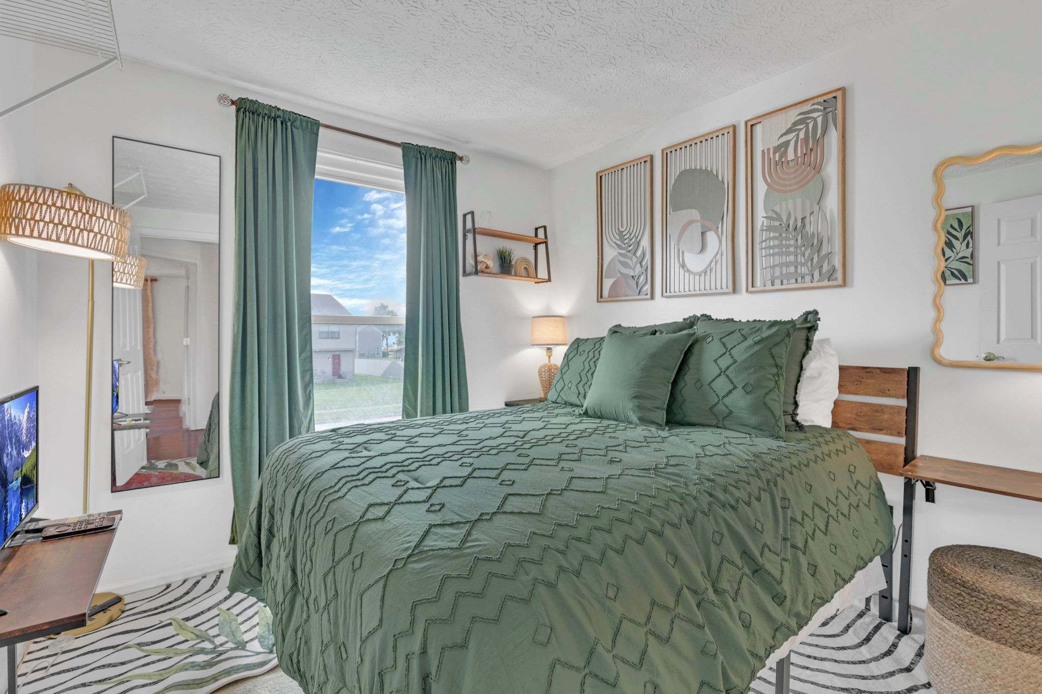 A bedroom with a bed, a television, a desk, and a window with curtains.