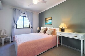 Ein Schlafzimmer mit einem Bett, einem Nachttisch, einer Lampe, einem Sessel und einem Fenster mit Vorhängen.