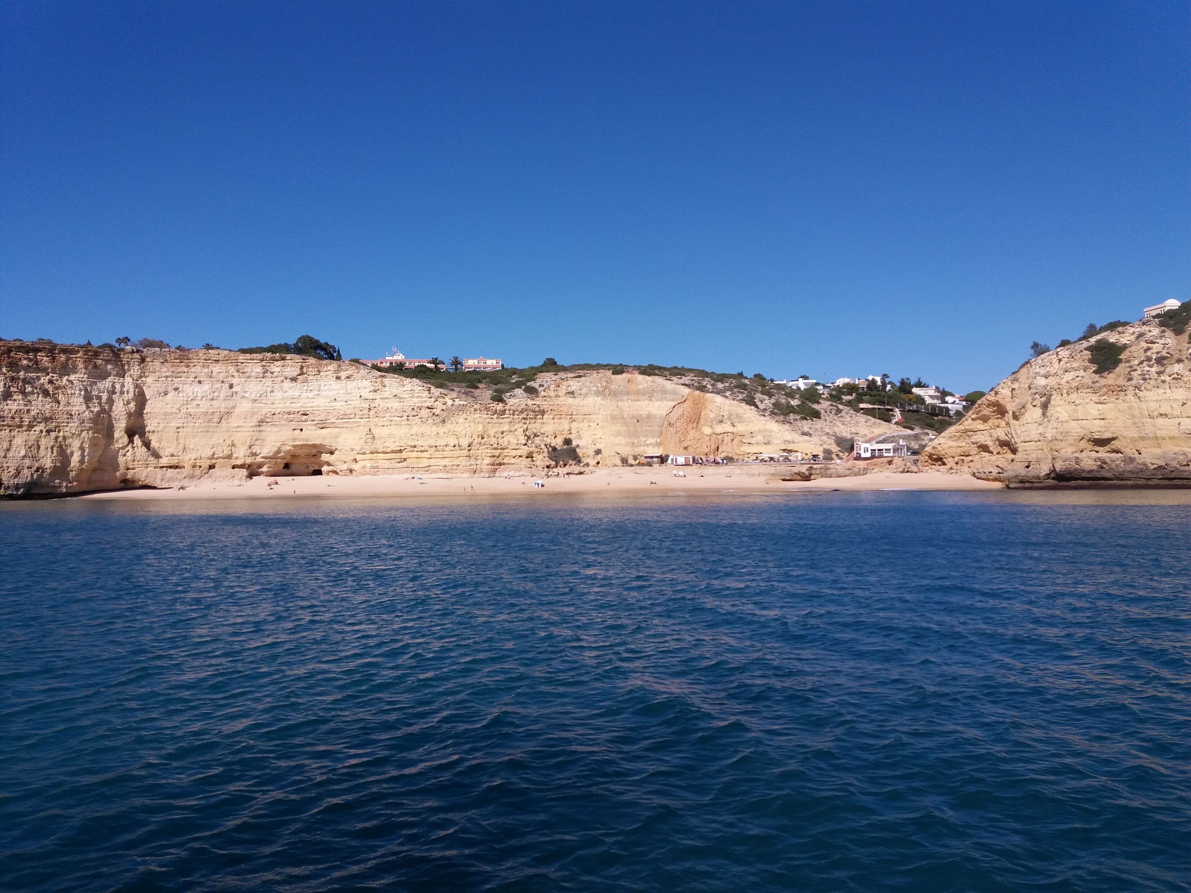 Paisaje costero con playa arenosa, acantilados rocosos y cielo azul despejado.