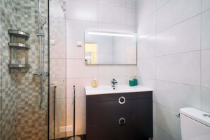 Uma casa de banho moderna com chuveiro, toucador com espelho e sanita.