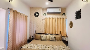 A bedroom with a bed, a ceiling fan, an air conditioner, and a floral-patterned chair. - House of Bindu (Udaipur)