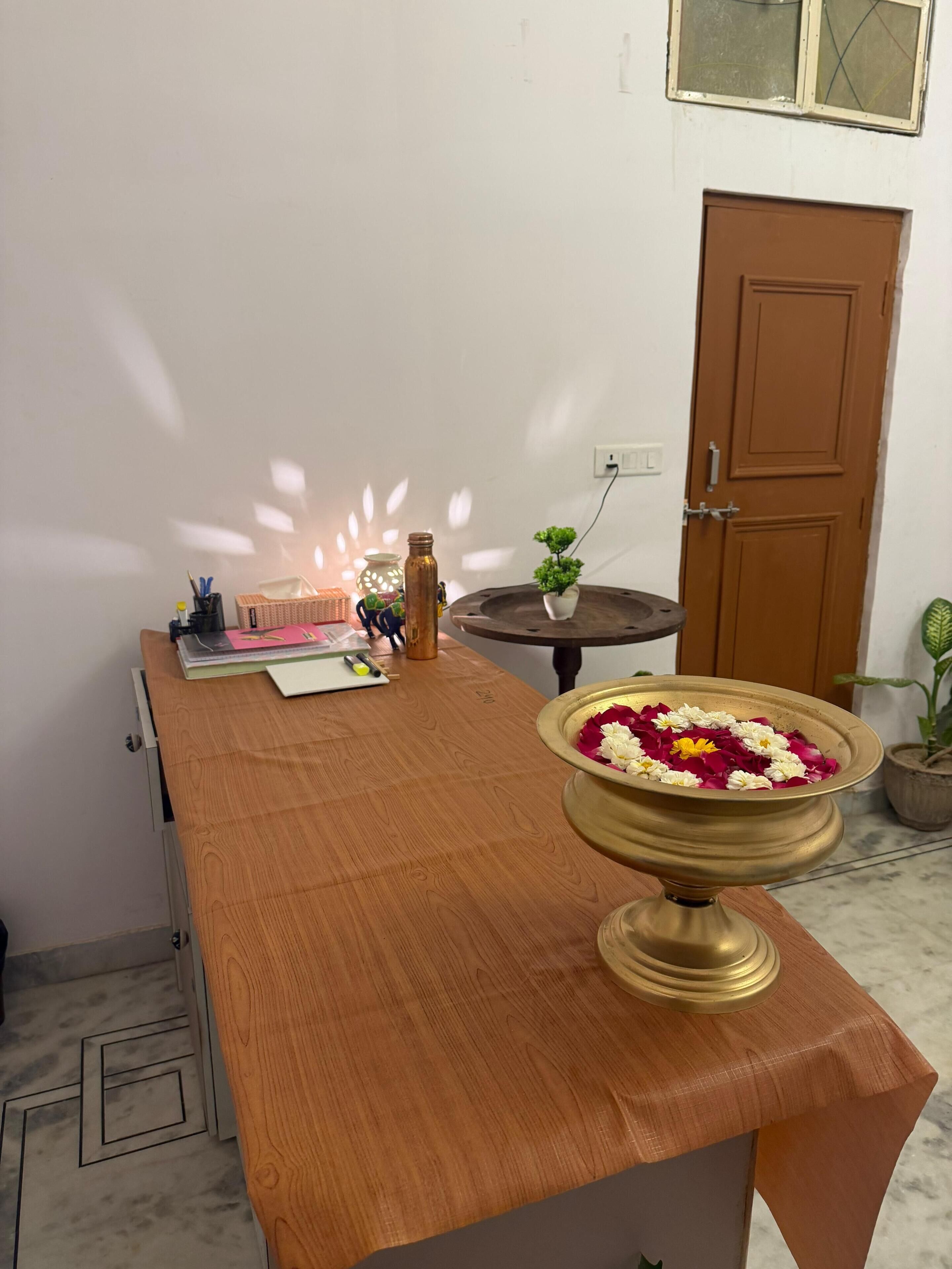 Un bureau en bois sur lequel se trouvent un bol en laiton rempli de fleurs, une bougie allumée et une plante en pot.