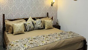 A bedroom with a bed, patterned wallpaper, wall sconces, a framed picture, and a decorative wall plate. - House of Bindu (Udaipur)