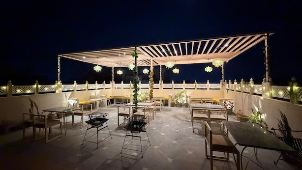 An outdoor patio area with tables and chairs, a pergola structure, and hanging lights. - House of Bindu (Udaipur)