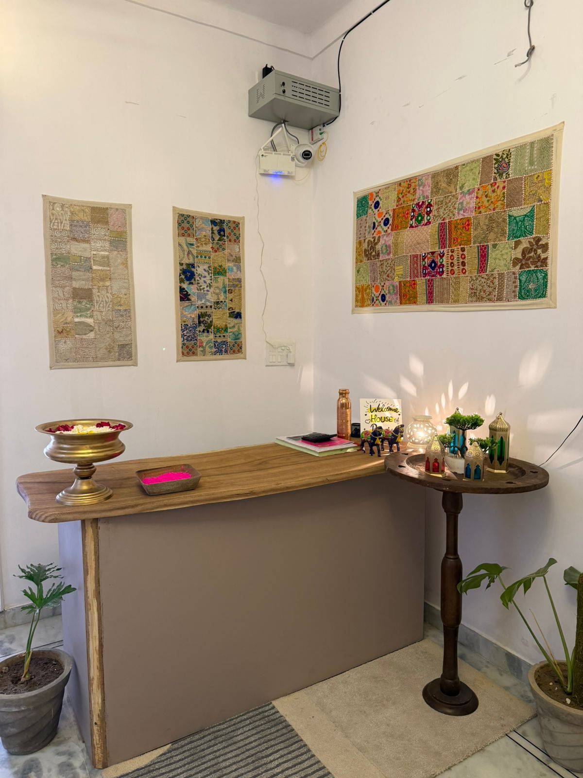 A room with a wooden reception desk, a projector mounted on the wall, and three quilted wall hangings.