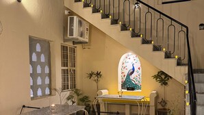 A staircase with a decorative railing, a dining area with a table and chairs, and a window with a peacock design. - House of Bindu (Udaipur)
