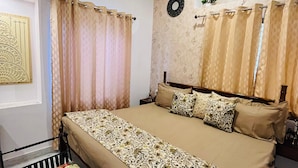 A bedroom with a bed, a bedside table, a ceiling fan, an air conditioning unit, and a wall-mounted light fixture. - House of Bindu (Udaipur)