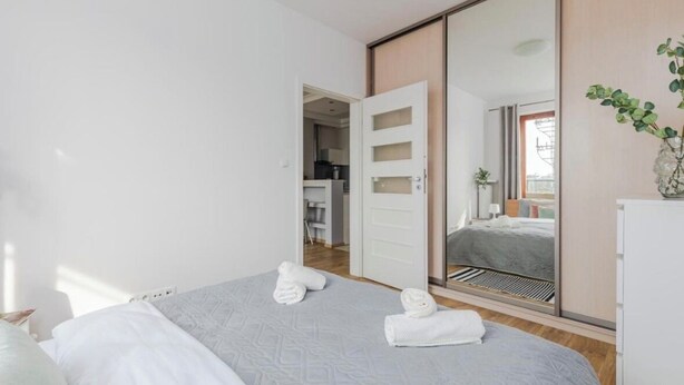 A hotel room with a bed, a wardrobe, a mirror, and a plant. - Kiedacza Apartament (Warszawa)