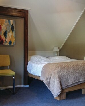 Ein Schlafzimmer mit einem Bett, einem Sessel, einer Lampe und einem farbenfrohen, abstrakten Gemälde an der Wand.