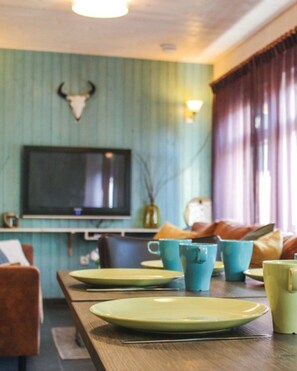 Ein Essbereich mit einem langen Tisch, Stühlen und einem an der Wand befestigten Fernseher.