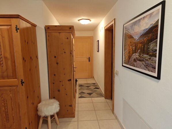 A hallway with wooden doors, a rug, a framed picture, and a small stool. - Cuntainta Champfer by Interhome (St. Moritz)