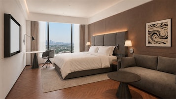 Una habitación de hotel moderna con una cama grande, un sofá, una mesita y vistas a la ciudad.