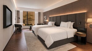Una habitación de hotel moderna con una cama grande, mesitas de noche, un escritorio y vistas a árboles por la ventana.