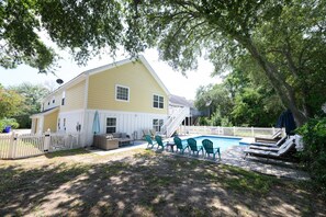 Une maison à deux étages avec une piscine, un espace salon extérieur et une cour clôturée.