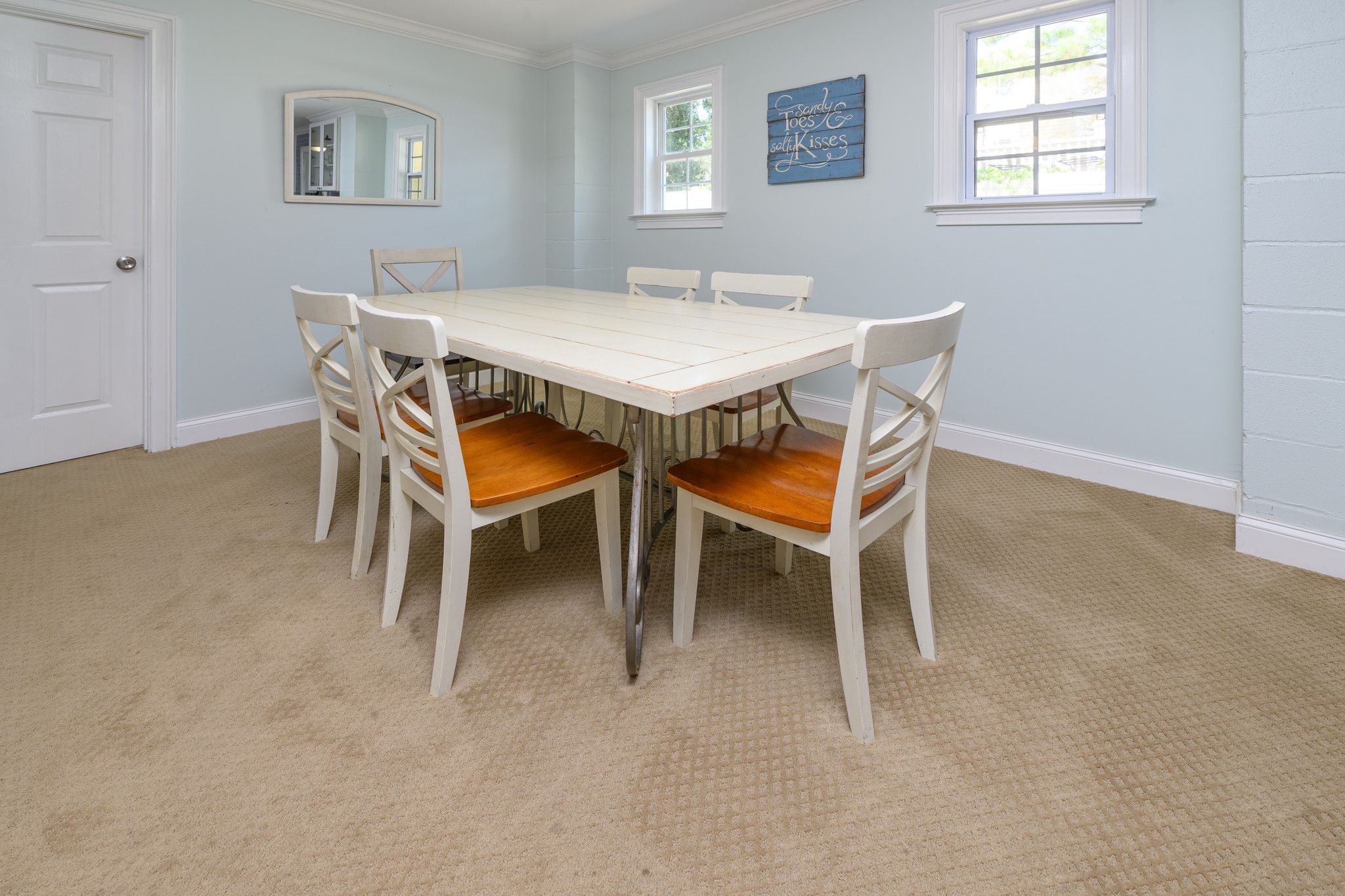 Une salle à manger avec une table et des chaises blanches, un sol recouvert de moquette et deux fenêtres.