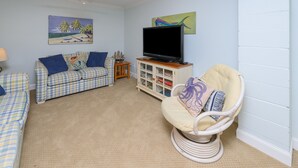 Ein Wohnzimmer mit Fernseher, zwei Sofas, einem Sessel und einem Bücherregal.