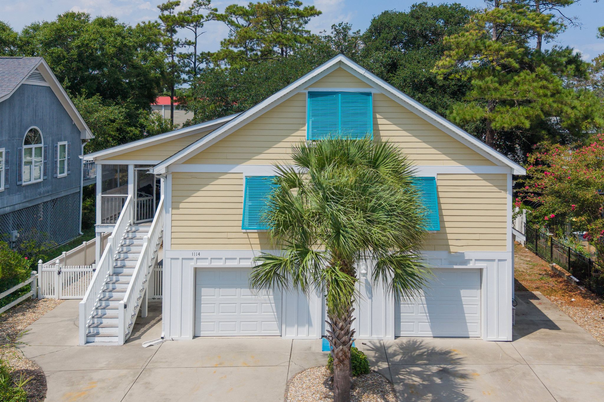 A two-story house with a front porch, a garage, and a palm tree in the front yard.