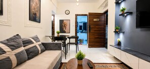 A modern living room with a sofa, a coffee table with a plant, a dining area with chairs, and a kitchen with a TV.