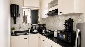 A kitchen with white cabinets, a black countertop, a coffee maker, and a stainless steel refrigerator.