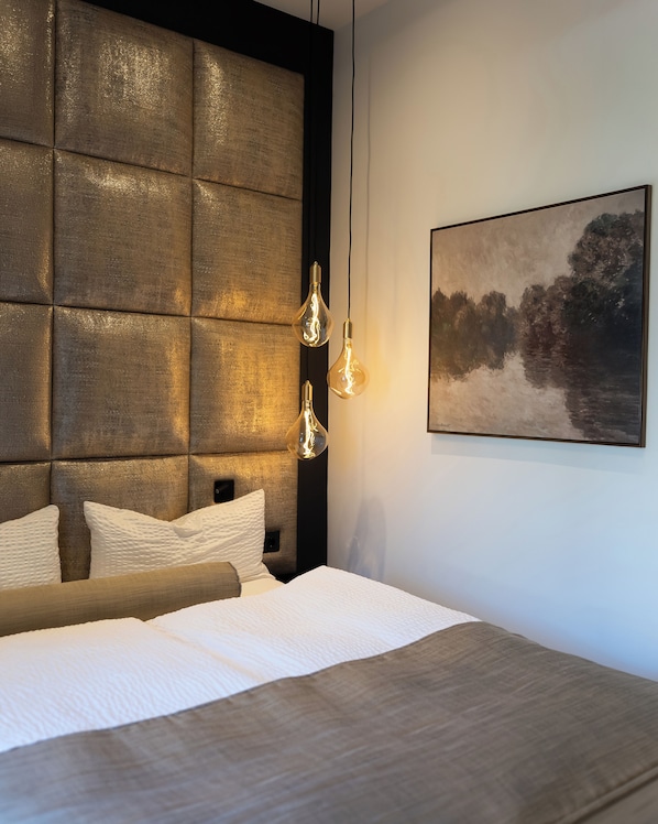 A modern bedroom with a tufted headboard, a large bed, and a landscape painting on the wall.