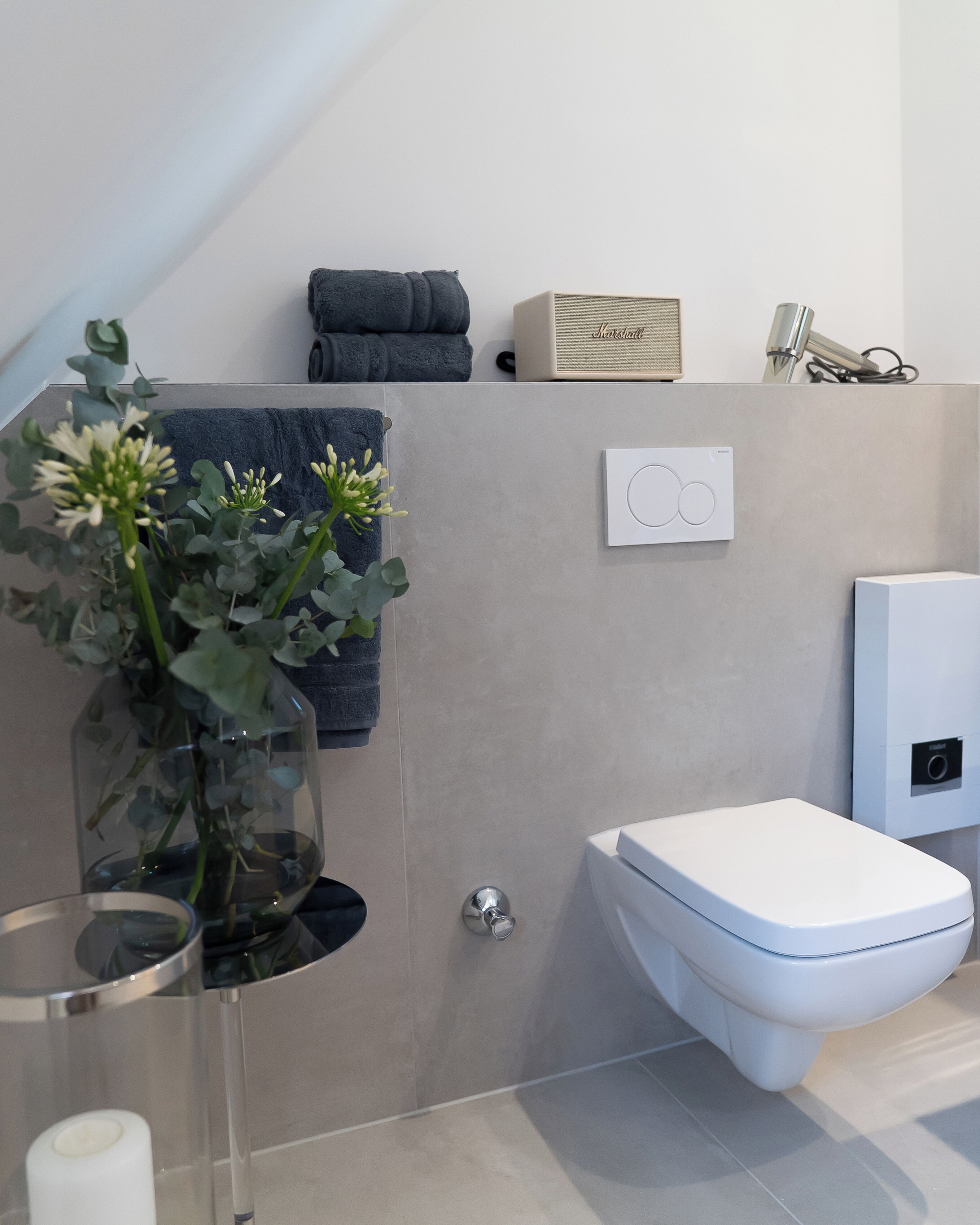 A modern bathroom with a toilet, a towel rack, a small plant, and a shower area.