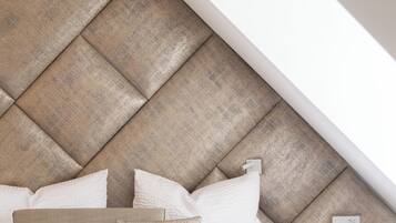 A bedroom with a sloped ceiling, a bed with white bedding, and a headboard made of wooden panels.