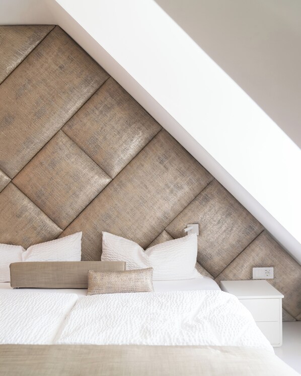 A bedroom with a sloped ceiling, a bed with white bedding, and a headboard made of wooden panels.