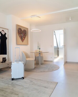 A modern living room with a white sofa, a small round table, a white floor lamp, and a heart-shaped artwork on the wall.