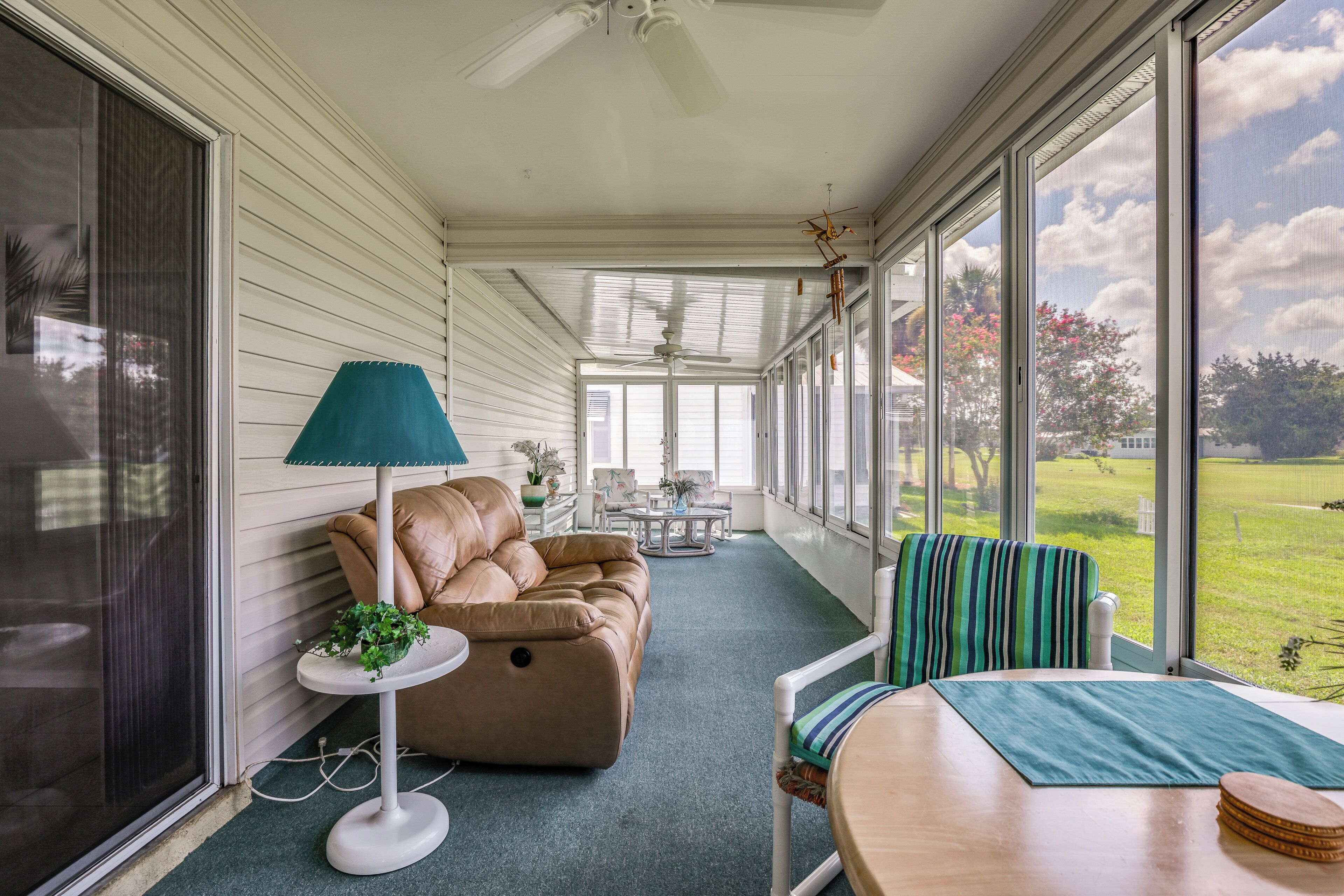 A covered porch with a sofa, a table, and chairs, overlooking a grassy area.