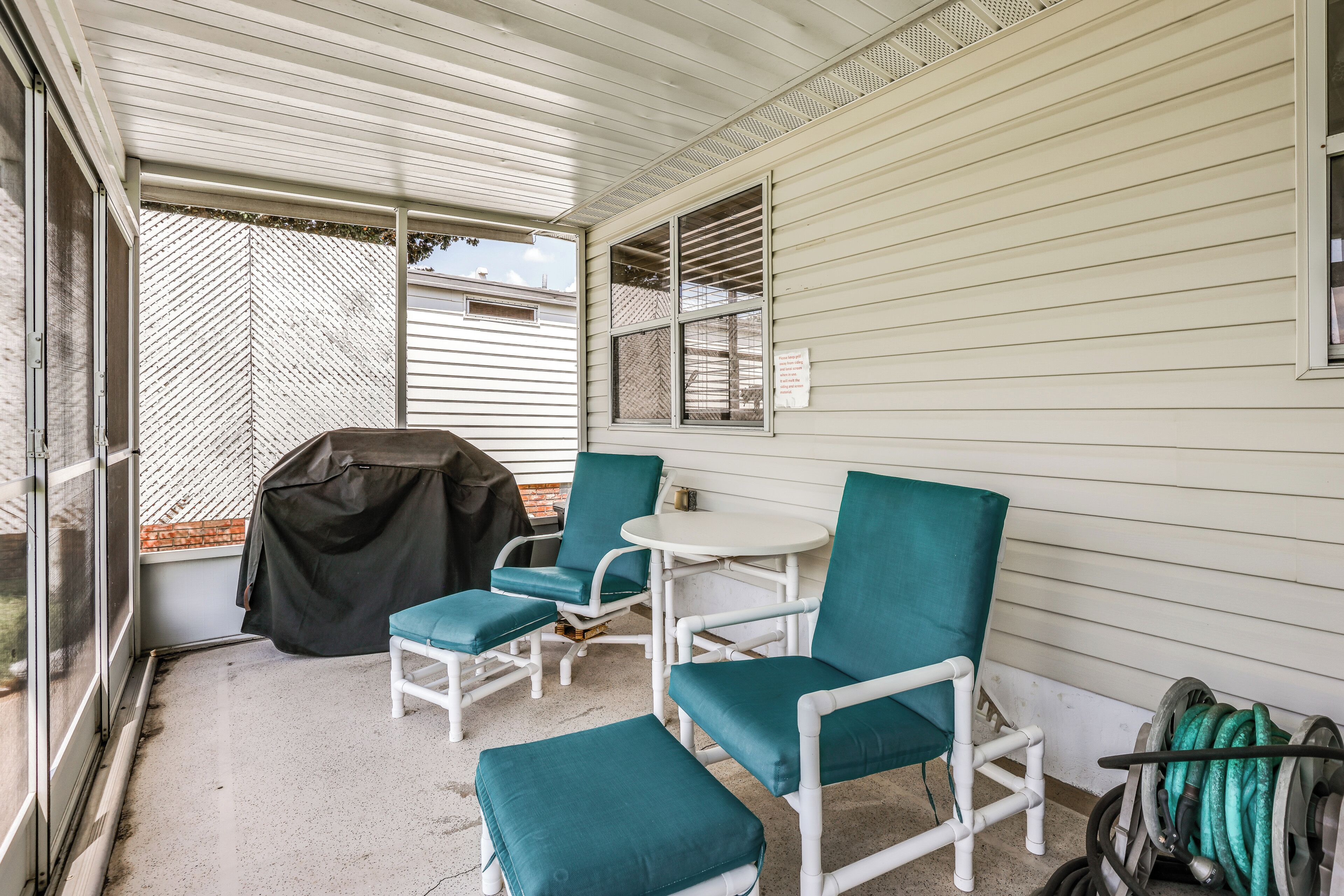 A covered patio area with a table and chairs, a grill, and a hose.