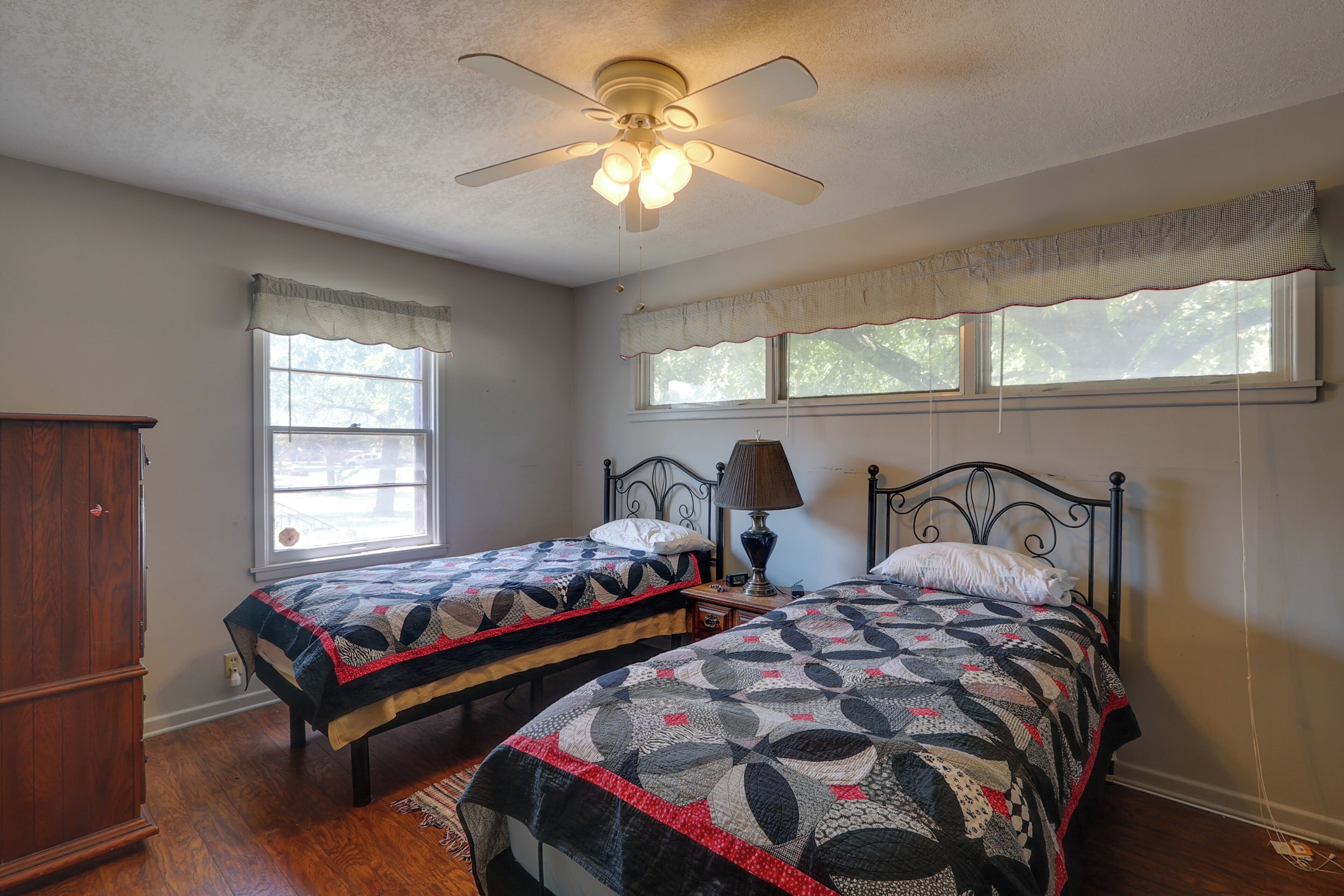 A bedroom with two beds, a ceiling fan, a window with a view, and a wooden wardrobe.