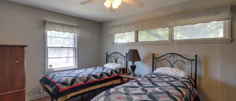 Une chambre avec deux lits, un ventilateur de plafond, une fenêtre avec vue et une armoire en bois.