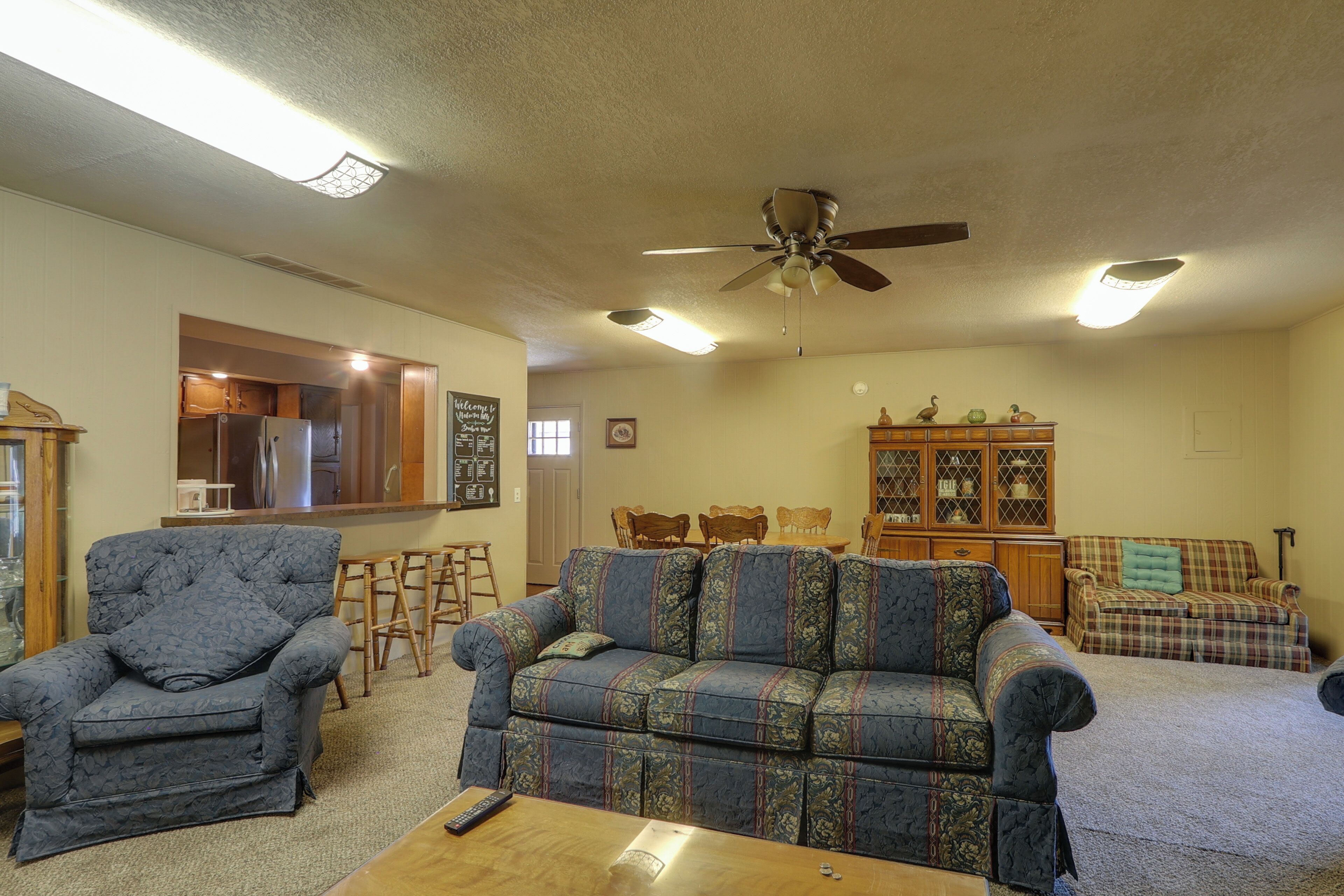 A living room with a sofa, armchairs, a coffee table, a ceiling fan, and a cabinet.