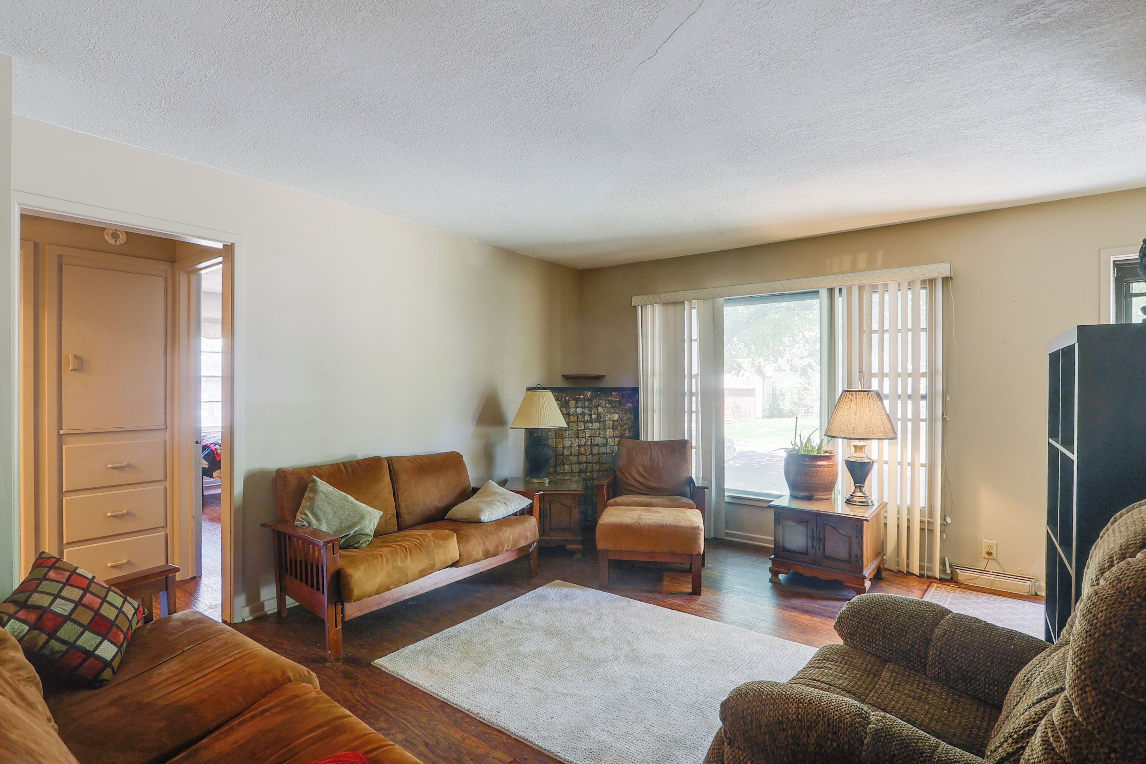 A living room with a brown leather sofa, a wooden chair, a small table with a lamp, and a stone fireplace.
