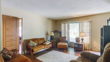 A living room with a brown leather sofa, a wooden chair, a small table with a lamp, and a stone fireplace.