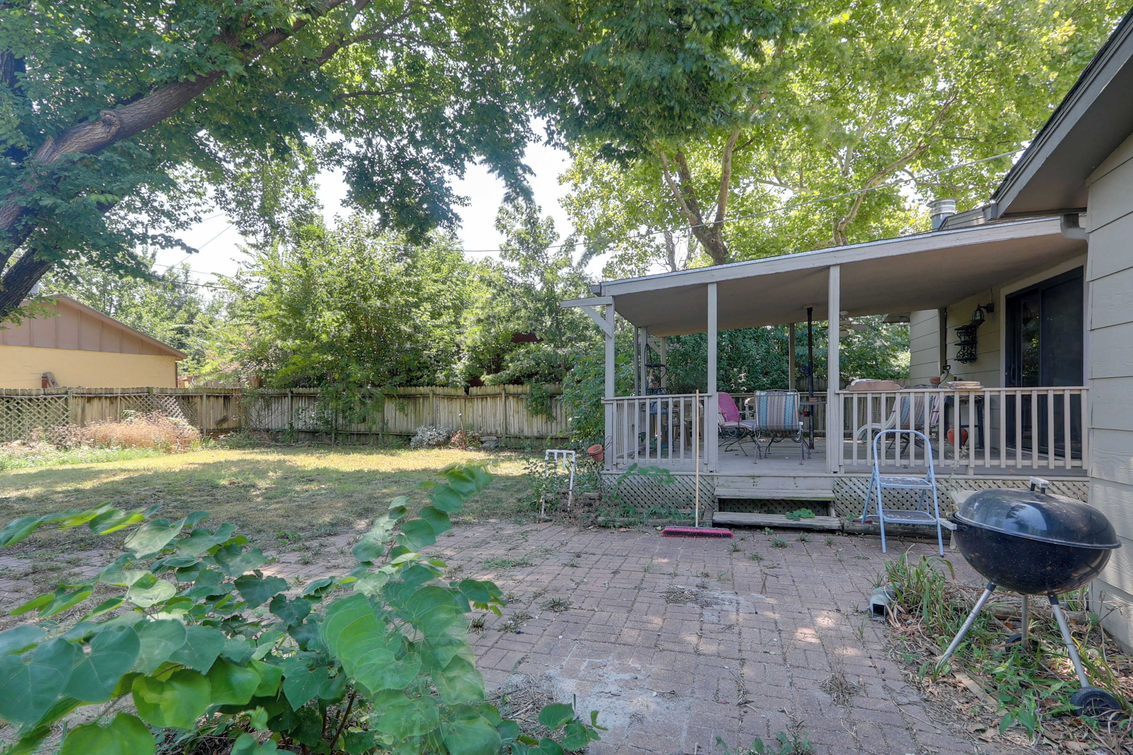 A backyard with a covered patio, a barbecue grill, and a wooden fence.
