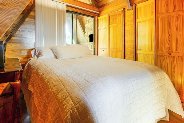 A bedroom with a large bed, wooden walls, and a window.