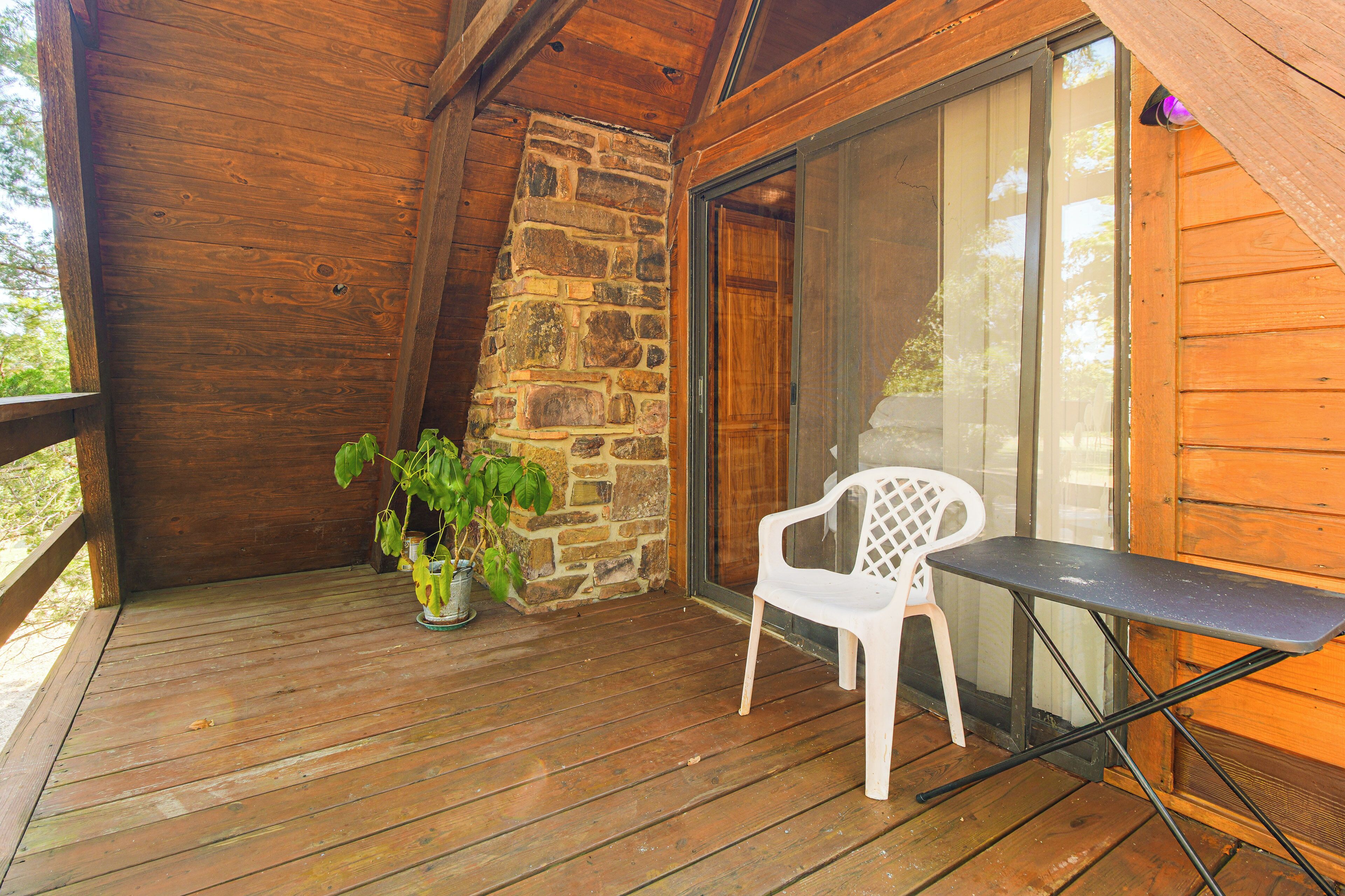 A wooden deck with a stone wall, a potted plant, a white plastic chair, and a table.