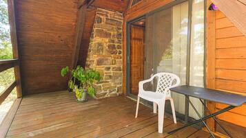 A wooden deck with a stone wall, a potted plant, a white plastic chair, and a table.