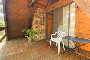 A wooden deck with a stone wall, a potted plant, a white plastic chair, and a table.
