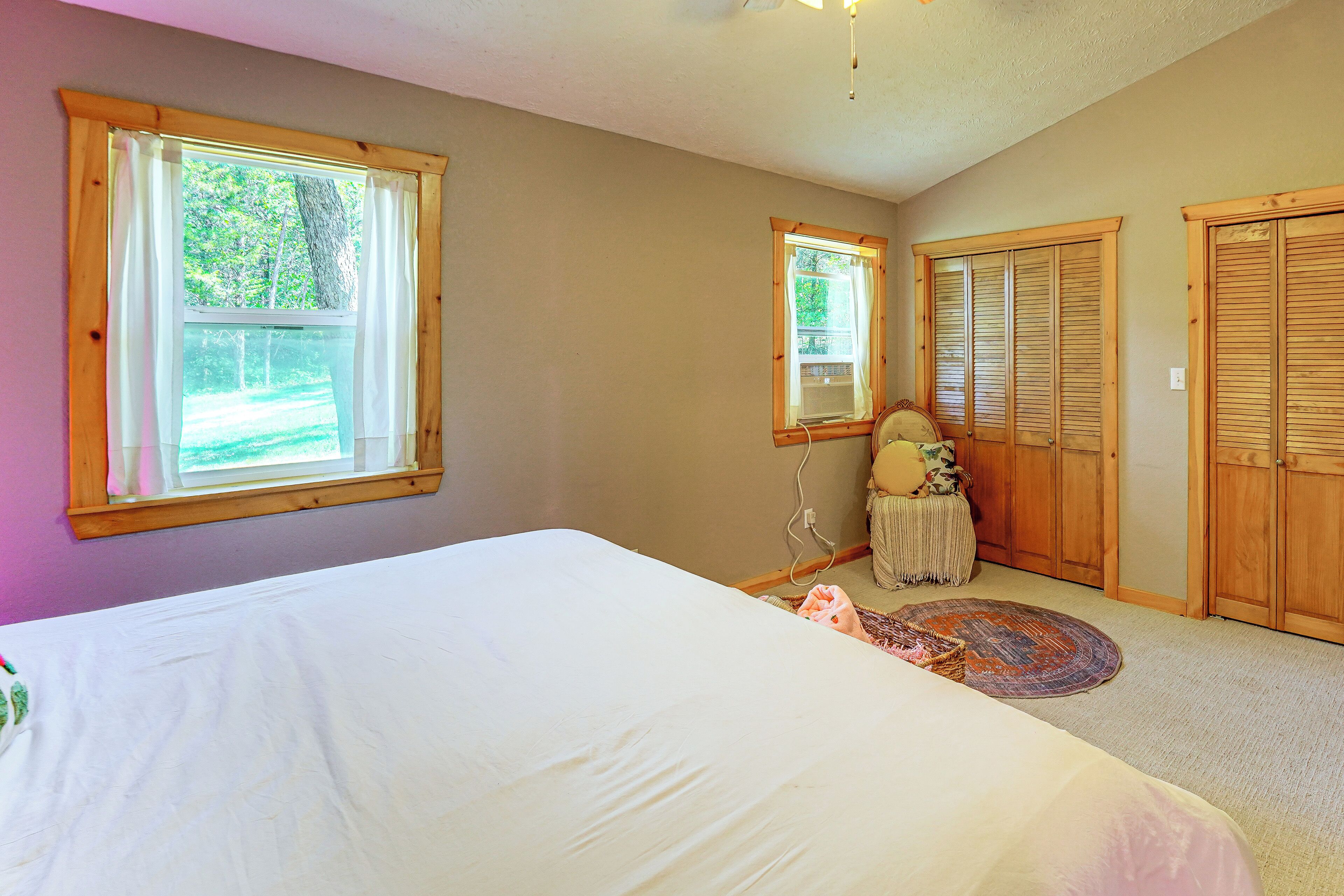 A bedroom with a bed, two windows, a wardrobe, and a small table with a chair.